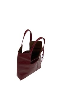 Borsa a mano in pelle borgogna con due manici, design aperto in cima, tasca interna e charm decorativo in perline su un lato. Texture liscia e forma strutturata.
