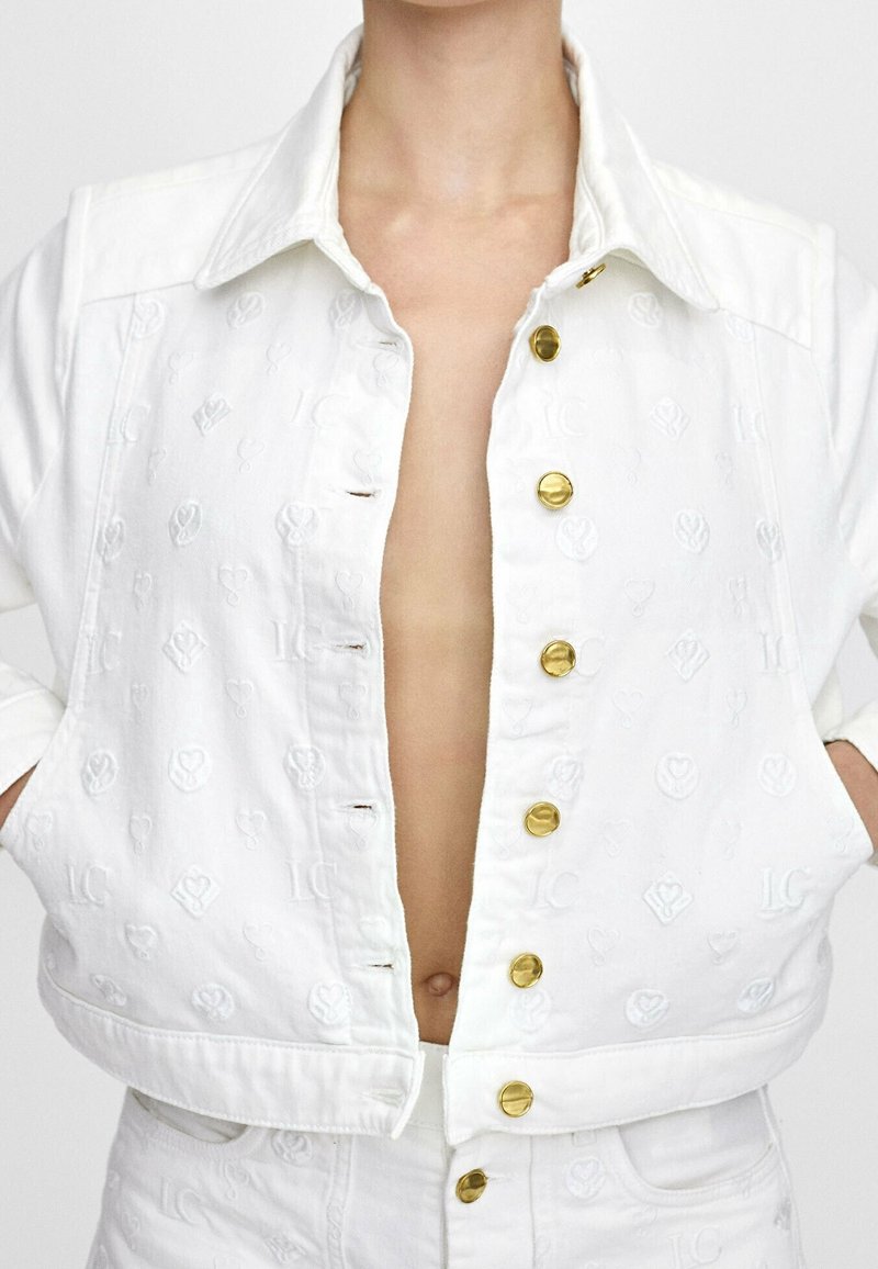 Vit kort jeansjacka med broderade mönster, guldfärgade knappar, spetsig krage och avslappnad passform.