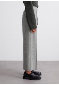 Grijze geruite wijde broek van textiel, gecombineerd met zwarte plateau-loafers. Zichtbare zijnaad en tailleband detail.