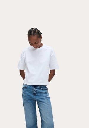 T-shirt en coton blanc avec un col rond et des manches courtes, associé à un jean en denim bleu clair. Design simple et décontracté.