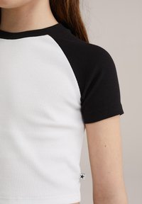 Top de manga corta con cuerpo blanco y mangas negras con canalé. Presenta una pequeña etiqueta con un detalle de estrella en el dobladillo.
