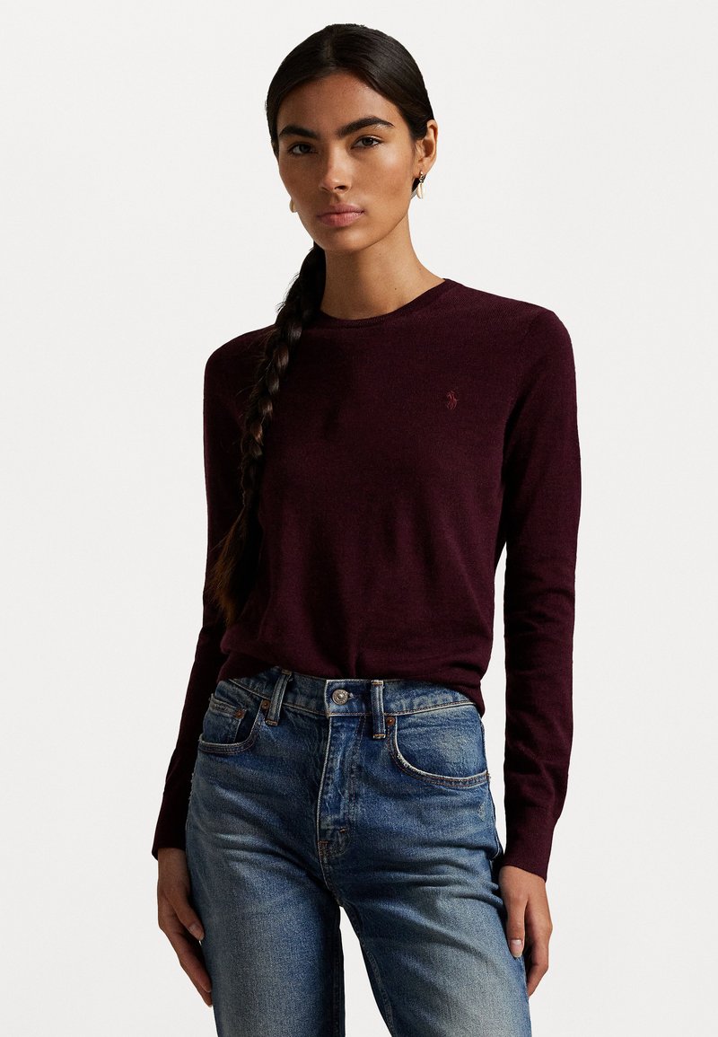 Haut en tricot bordeaux à manches longues avec un col rond et un détail de logo subtil, associé à un jean en denim bleu avec une coupe classique et une taille haute.