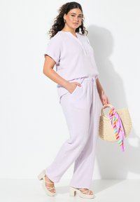 Lila, lichtgewicht, ongevoerd tweedelig set bestaande uit een kortmouw button-up top en losse broek, aangevuld met een geweven tas met kleurrijke linten.