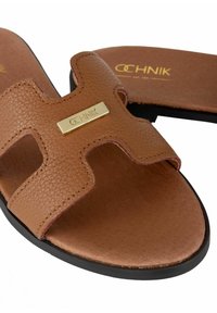 Brązowe skórzane sandały wsuwane z teksturowanym wykończeniem, z złotą plakietką logo i gładką wkładką. Czarna podeszwa bez widocznego wzoru.