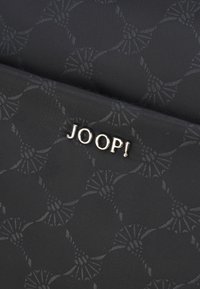 Svart tyg med ett texturerat mönster, med en metallisk guld "JOOP!"-logga accentuerad på ytan.