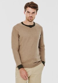 Beżowy sweter z długim rękawem i dekoltem w kształcie litery V, z ciemnozielonym prążkowanym kołnierzem i mankietami, wykonany z miękkiej, teksturowanej dzianiny.