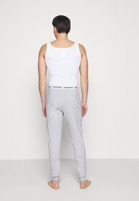 Witte tanktop en grijze sweatpants met een zwarte tailleband, met het "BJÖRN BORG" logo, gezien vanaf de achterkant. Zachte stoftextuur, casual pasvorm.