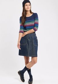 Top a maniche lunghe a righe blu navy con strisce multicolore, abbinato a una gonna di denim scuro con due tasche frontali e bottoni. Beanie blu navy e calzini.