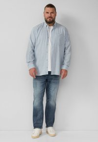 Lichtblauw geruit shirt met button-down kraag, gedragen over een wit T-shirt, gecombineerd met lichtblauwe jeans en witte sneakers.