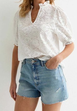 Vrouw draagt een witte eyelet kanten blouse met pofmouwen en lichtblauwe high-waisted denim shorts met rafelige zoom.