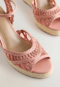 Sandales compensées ouvertes rose avec des brides tressées et une semelle en jute tissée sur un fond clair.