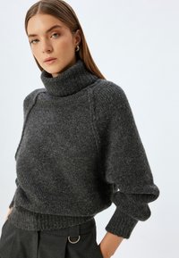 Donkergrijs gebreid coltrui met geribbelde textuur, losse pasvorm en verlaagde schouders, gecombineerd met hooggetailleerde donkere broek.