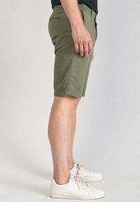 Olijfgroene shorts van katoen, met een rechte snit, zijzakken en licht omgeslagen zomen. Gemaakt met witte veterschoenen.