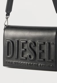 Μαύρο δερμάτινο τσάντα ώμου με ανάγλυφο λογότυπο "DIESEL" και το σύνθημα "FOR SUCCESSFUL LIVING", εξοπλισμένη με αποσπώμενο άγκιστρο ιμάντα.