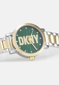 Ceas DKNY cu un cadran texturat verde, accente aurii și brățară din oțel inoxidabil argintiu. Prezentă marcaje cu cristale și logo în centru.