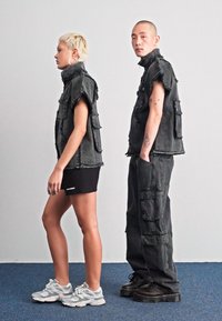 Δύο μοντέλα φορούν μαύρα, φθαρμένα τζην γιλέκα με πολλαπλές τσέπες. Το ένα το συνδυάζει με μια μαύρη φούστα, ενώ το άλλο με cargo παντελόνια και χοντρές μπότες.