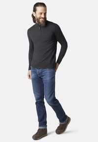 Donkergrijze sweater met rits, slim-fit blauwe spijkerbroeken en bruine wandelschoenen. De sweater heeft een geribbelde zoom; de jeans hebben een klassieke snit.