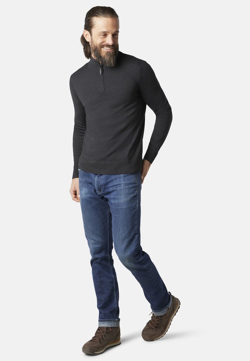 Donkergrijze sweater met rits, slim-fit blauwe spijkerbroeken en bruine wandelschoenen. De sweater heeft een geribbelde zoom; de jeans hebben een klassieke snit.