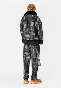 Chaqueta negra y gris con un patrón y cuello de piel, combinada con pantalones a juego que tienen una etiqueta lateral y acentuada con botas gruesas naranjas.