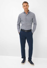 Camicia a maniche lunghe, con bottoni, a stampa blu e bianca, abbinata a chinos blu e sneakers scure. Presenta un colletto classico e una vestibilità slim.