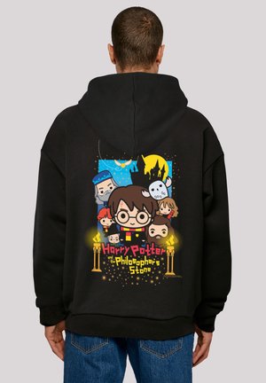 Svart hettegenser med fargerike tegneseriefigurer fra "Harry Potter og De vises stein" på baksiden, avtegnet mot en blå bakgrunn.