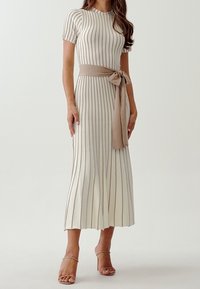 Robe en tricot côtelé, jusqu'aux genoux, en crème avec de subtiles rayures verticales et une ceinture beige nouée à la taille ; manches courtes, jupe évasée.