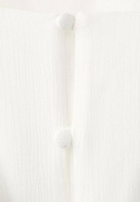 Dva malé kulaté knoflíky potažené látkou na texturované bílé látce, uspořádané vertikálně.