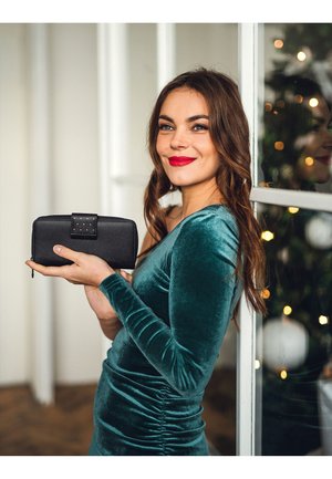 Black leather wallet with a textured finish and a studded strap detail, held in a hand against a blurred background with soft lighting.