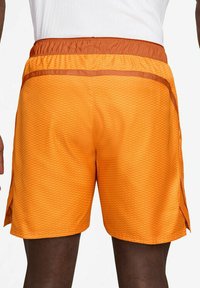 Orange Sportshorts mit einem strukturierten Rautenmuster, ausgestattet mit einem elastischen Bund und seitlichen Schlitzen für mehr Bewegungsfreiheit.