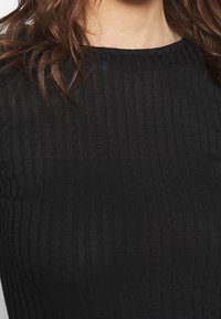 Czarna, prążkowana bluzka z dzianiny z okrągłym dekoltem. Materiał jest miękki i dopasowany, z wyraźnymi pionowymi paskami na całej powierzchni.