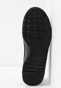 Semelle de chaussure Nike noire avec des motifs de bande de roulement carrés et linéaires, légèrement inclinée sur un fond blanc d’angle.