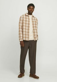 Checkered plaid shirt in beige and cream tones, button-up design, paired with a cream sweater and brown trousers. Brown lace-up shoes.