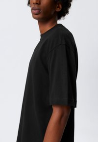 Sort bomulds t-shirt med korte ærmer, rund hals og løs pasform. Glat tekstur og minimal synlig syning.