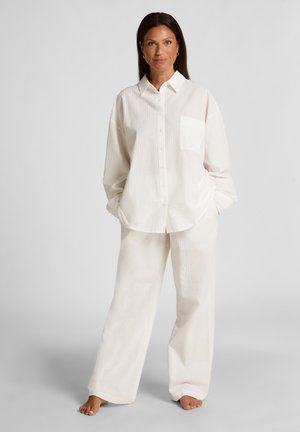 White button-up shirt with a pocket and textured pattern, paired with matching loose-fit pants in a soft fabric, worn barefoot.