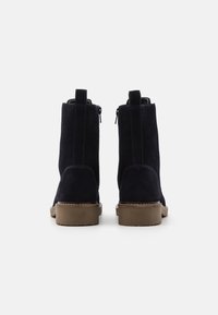 Botas de tobillo de ante en azul marino oscuro con una textura suave, dos cremalleras laterales y una suela de goma marrón resistente.