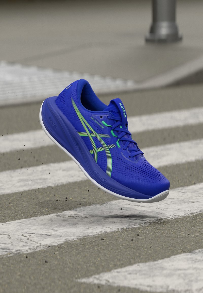 Μπλε αθλητικό παπούτσι με πράσινες ρίγες στον αέρα πάνω από διάβαση πεζών σε πλακόστρωτο δρόμο.