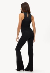 Un bodysuit negro con cuello alto y espalda con abertura, combinado con pantalones acampanados negros ajustados que cuentan con sutiles bolsillos traseros.