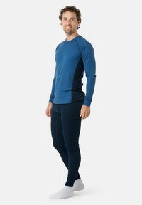 Haut bleu à manches longues en tissu ribé texturé, associé à des leggings navy ajustés. Caractéristiques des panneaux d'épaule contrastants et un col rond.