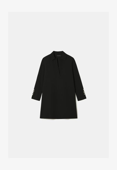 Robe tunique noire avec un col, décolleté en V profond et manches trois-quarts avec des accents de bouton au niveau des poignets. Texture lisse.