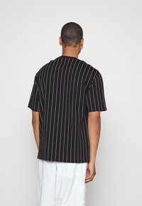 Black striped short-sleeve shirt featuring white vertical stripes, smooth texture, relaxed fit, and a round neckline.