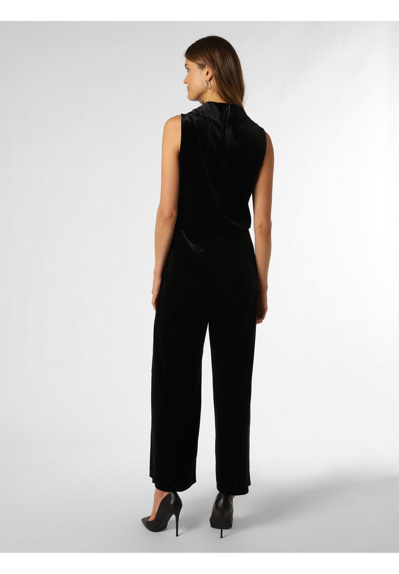 Schwarzer Samtjumpsuit mit ärmellosem Design, weitem Bein und glatter Textur. Das Model trägt schwarze High Heels und präsentiert einen klaren, minimalistischen Look.