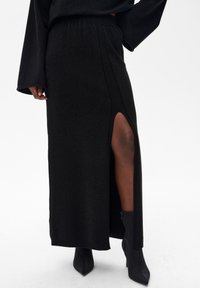 Czarna dzianinowa spódnica maxi z bocznym rozcięciem, o fakturowanym wykończeniu i elastycznym pasie. Noszona z czarnymi, szpiczastymi botkami za kostkę.