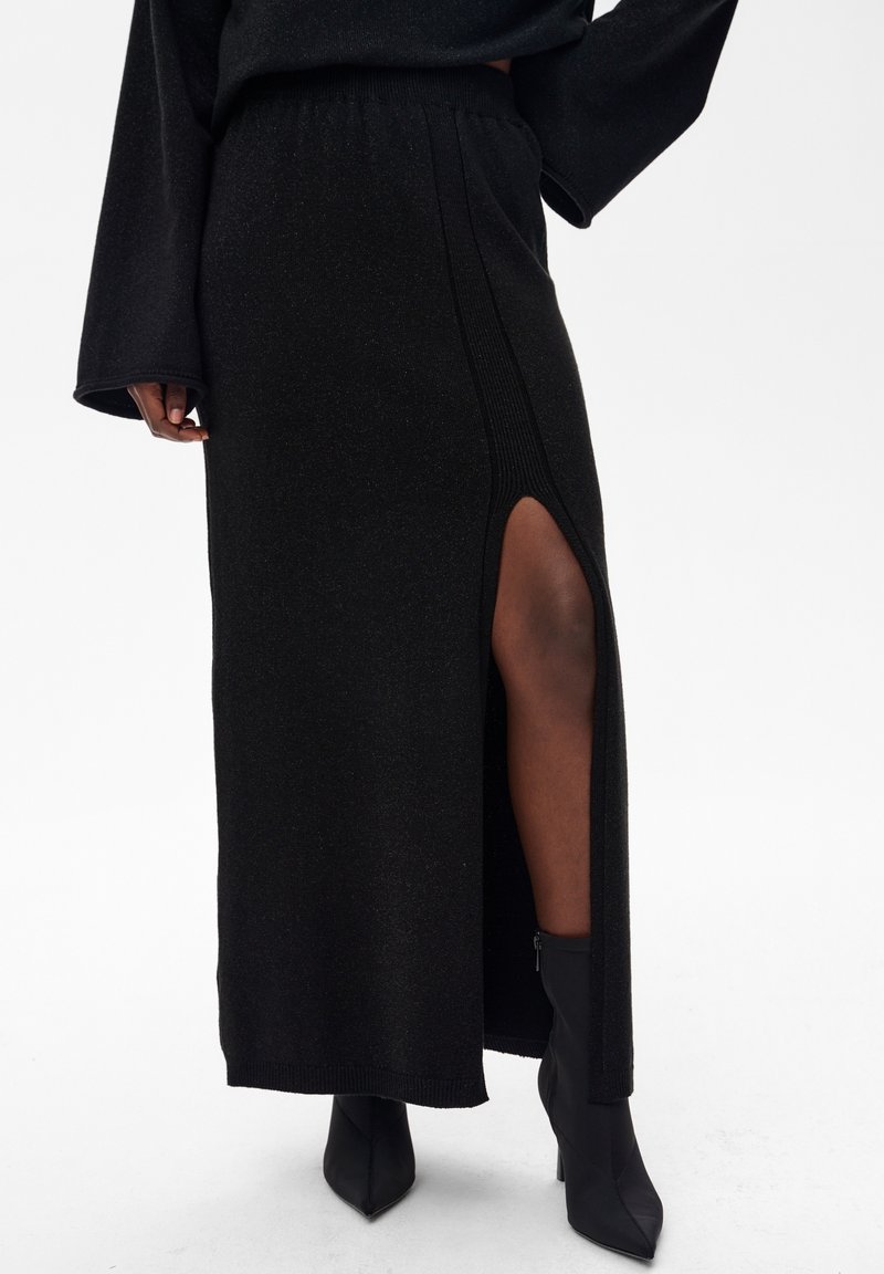 Czarna dzianinowa spódnica maxi z bocznym rozcięciem, o fakturowanym wykończeniu i elastycznym pasie. Noszona z czarnymi, szpiczastymi botkami za kostkę.
