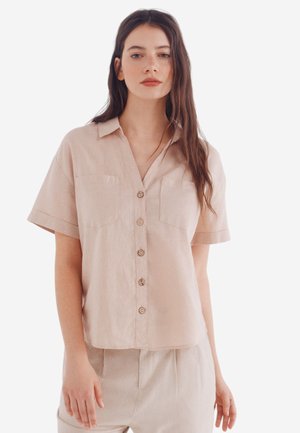 Short-sleeve, collared shirt in soft beige linen, featuring a button-down front and two chest pockets, with a relaxed, slightly cropped fit.