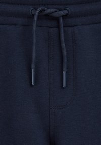 Tumši zili treniņbikses ar regulējamu jostasvietu, kurai ir plastmasas galiņi, mīksta tekstūra un sānu kabata ar smalku šuvuma detaļu.