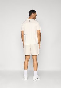 Light beige athletic T-shirt and shorts, featuring subtle blue accents and a smooth, lightweight fabric. Back view showing fit and design.