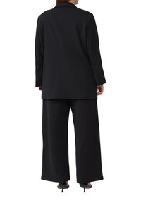 Zwarte op maat gemaakte blazer met lange mouwen en afgeknipte kraag, gecombineerd met wijde zwarte broek. Gladde textuur en eenvoudig ontwerp.