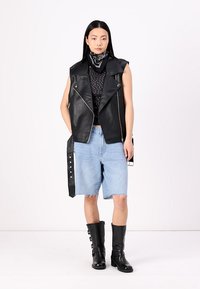 Črna usnjena brezrokavnik s srebrnimi zadrgami, v paru s črnim bluzončkom s pikicami, svetlimi modrimi jeans kratkimi hlačami in črnimi škornji do kolen.