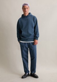 Marineblauwe hoodie met kangoeroe zak en geborduurde tekst, gecombineerd met bijpassende broeken en zwarte loafers. Zacht katoen materiaal; comfortabele pasvorm.