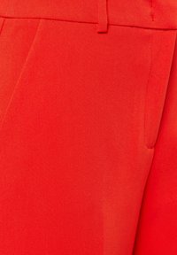 Red tailored trousers made from smooth fabric, featuring a tapered design, side pockets, and a subtle sheen with stitched details.